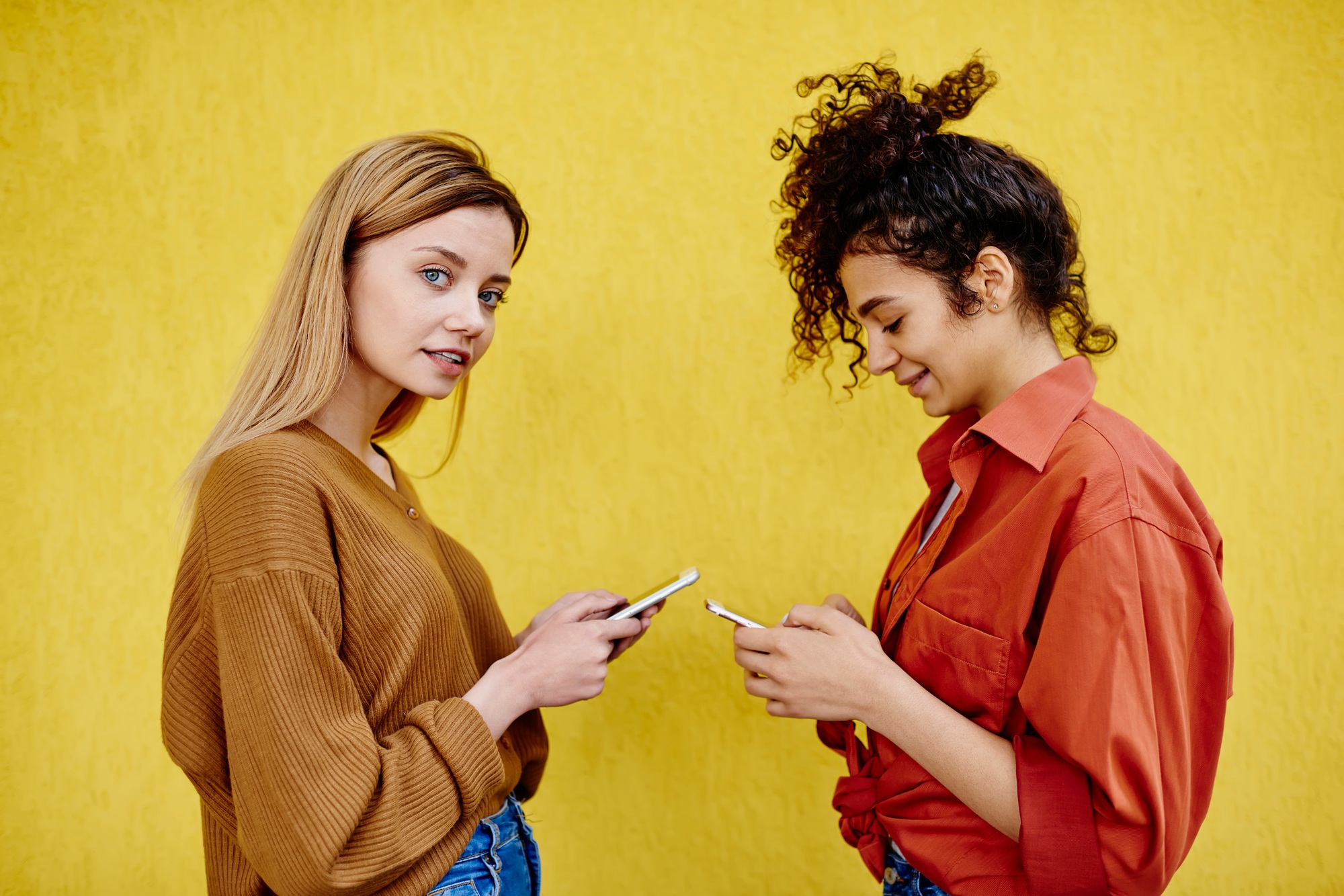 Dreamy female friends text messaging on smartphones